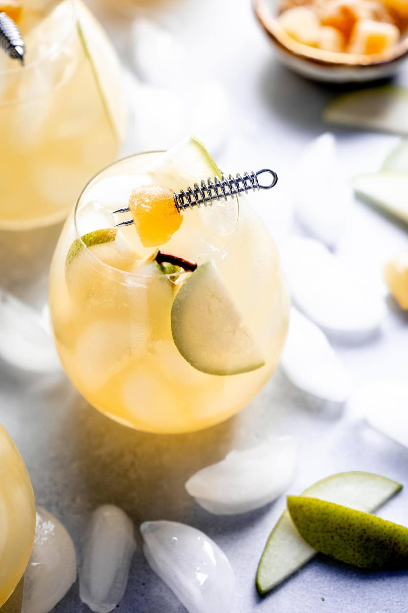 Three pear ginger sparkling cocktails spread on countertop with ice cubes and bowl of crystalized ginger.