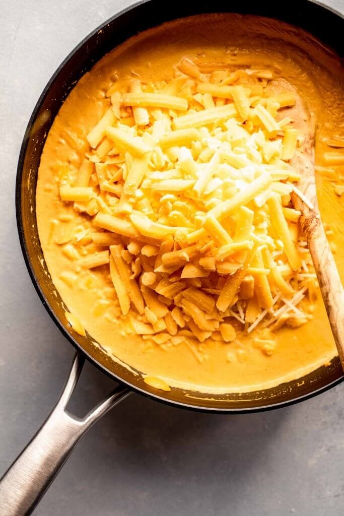 Cheese grated into skillet of pumpkin sauce.