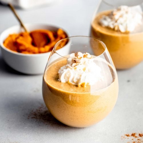 Side view of pumpkin pie smoothie next to small bowl of pumpkin puree.