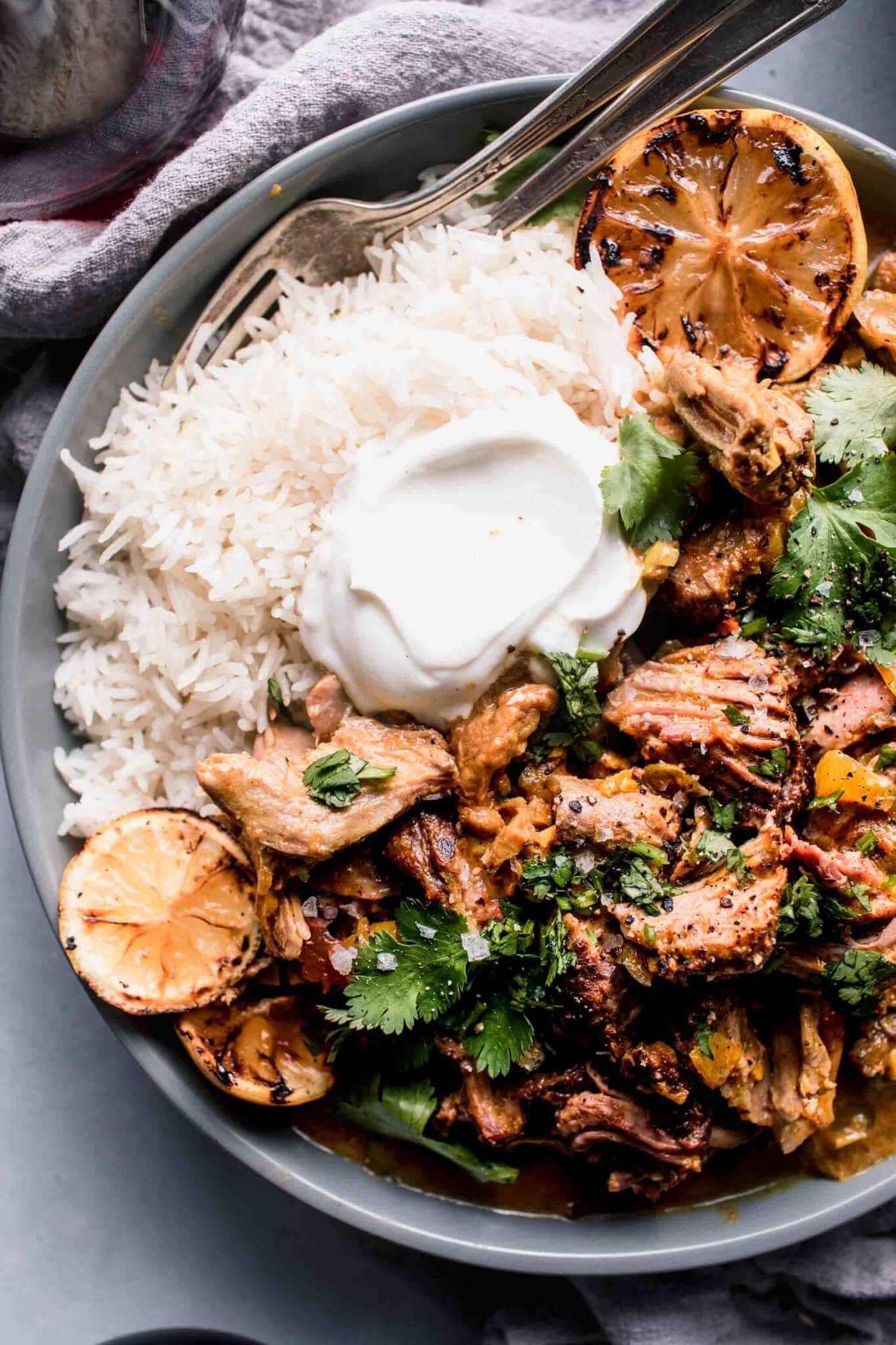 Overhead shot of bowl of lamb curry served over rice with dollop of yogurt and charred lemon slices.