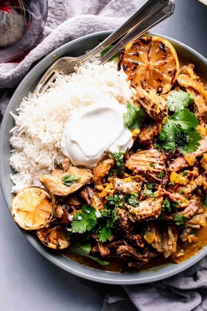 Overhead shot of bowl of lamb curry served over rice with dollop of yogurt and charred lemon slices.