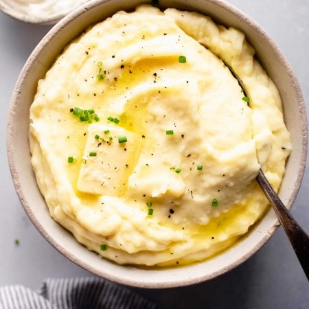 Overhead shot of bowl of mashed potatoes topped with a pat of butter, next to bowl of sour cream.