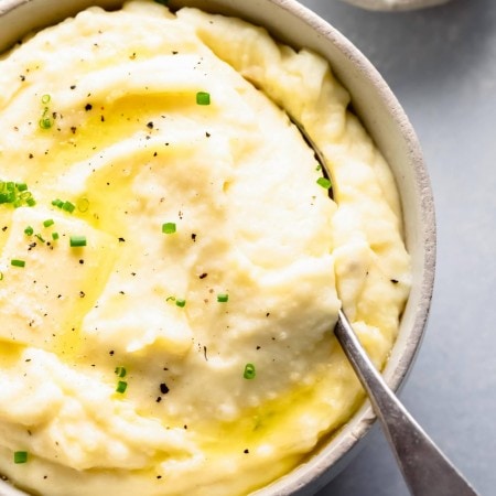 Overhead shot of bowl of mashed potatoes topped with a pat of butter, next to bowl of sour cream.
