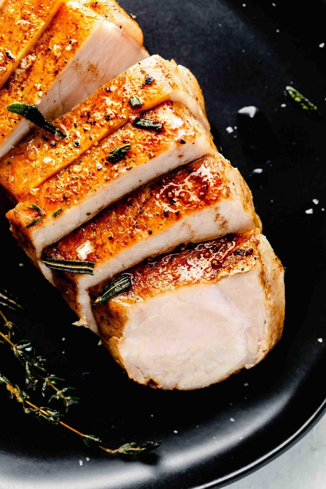 Sliced pork chop of black plate with scattered fried herbs.