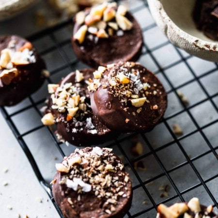 Chocolate shortbread cookies on cooling rack next to bowls of chocolate and sea salt.