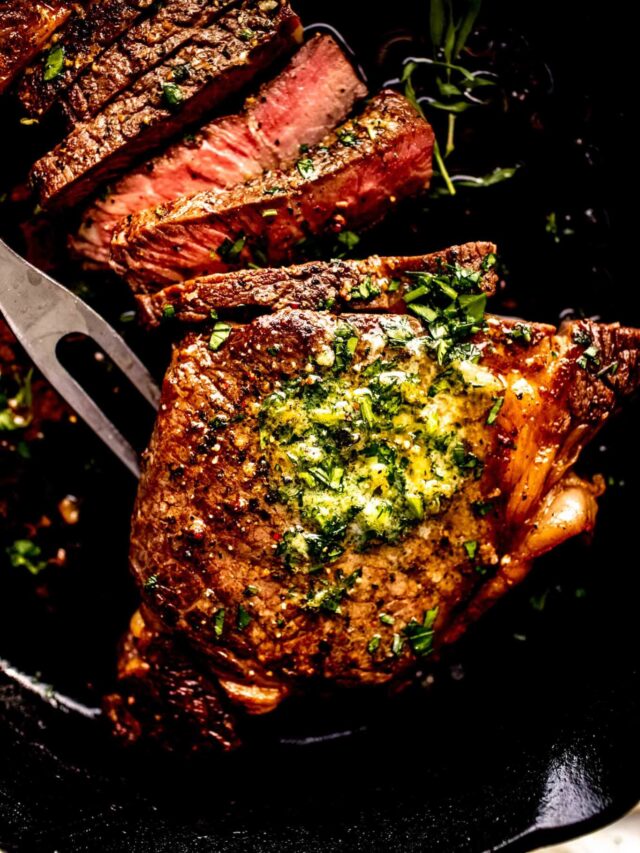 Seared ribeye in skillet sliced and topped with butter.