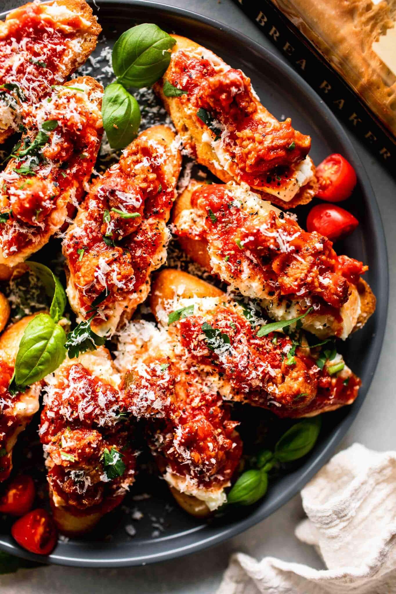 Overhead shot of crostini lasagna appetizer on grey plate next to white napkin.