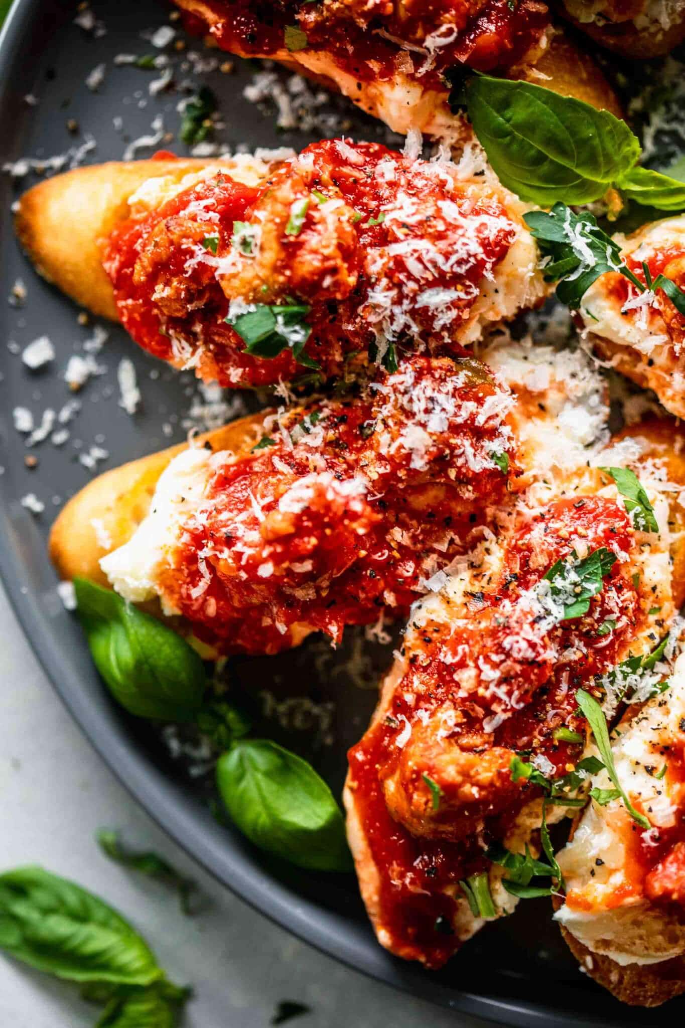 Close up of crostini lasagna appetizer on grey plate with basil leaves scattered about