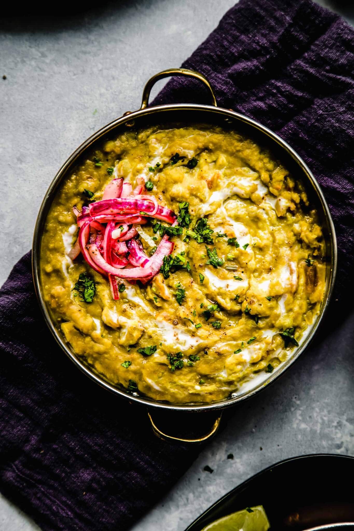 Overhead shot of dal topped with pickled onions in shallow bowl with handles.