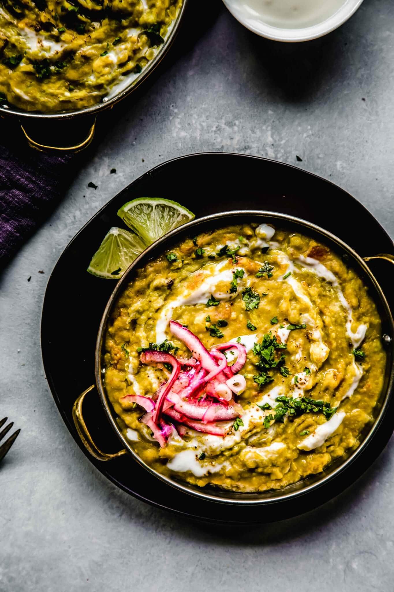 Two bowls of instant pot dal topped with onions and a swirl of yogurt. Served with limes. 