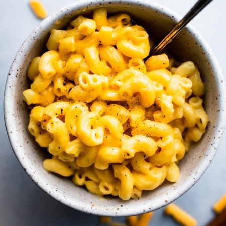 Overhead shot of mac and cheese in speckled bowl with spoon and grated cheddar scattered about.