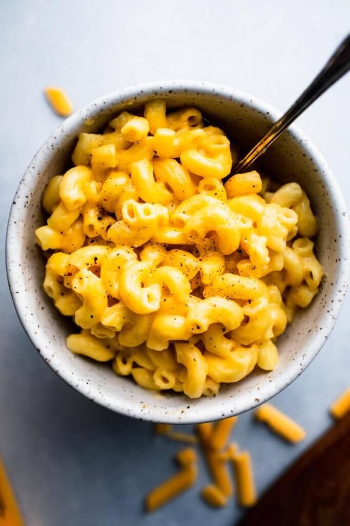 Overhead shot of mac and cheese in speckled bowl with spoon and grated cheddar scattered about.