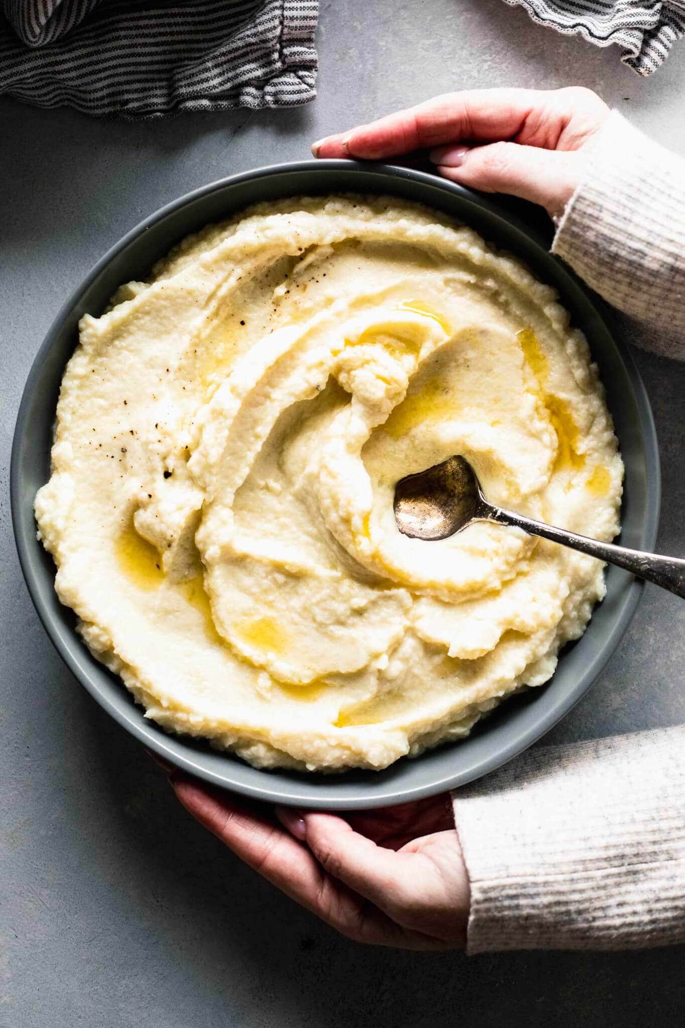 Two hands holding bowl of cauliflower mash. 