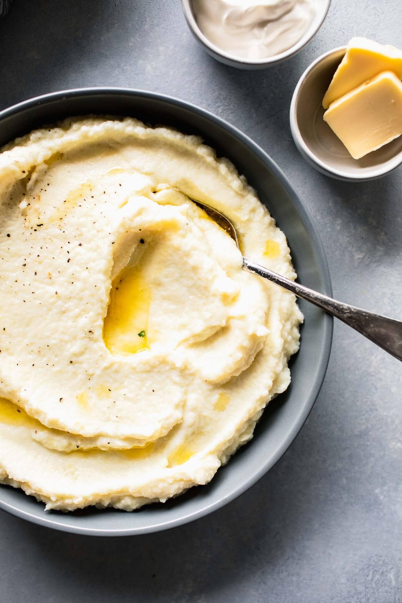 Overhead shot of cauliflower mash in bowl next to butter and sour cream.