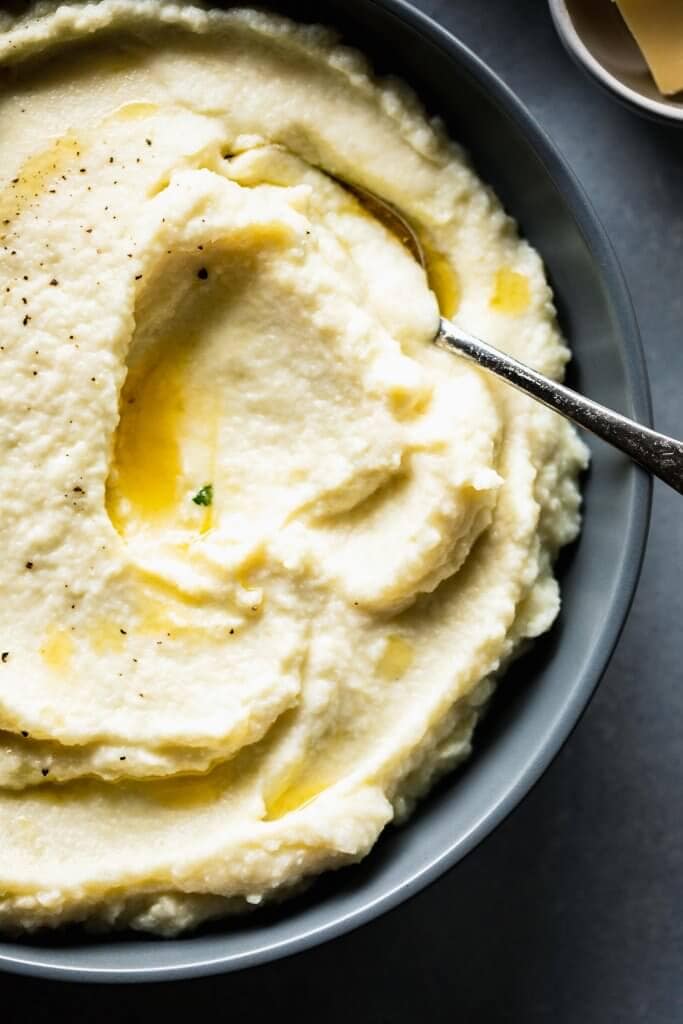 Overhead shot of bowl of mashed cauliflower in grey bowl with swirls of butter.