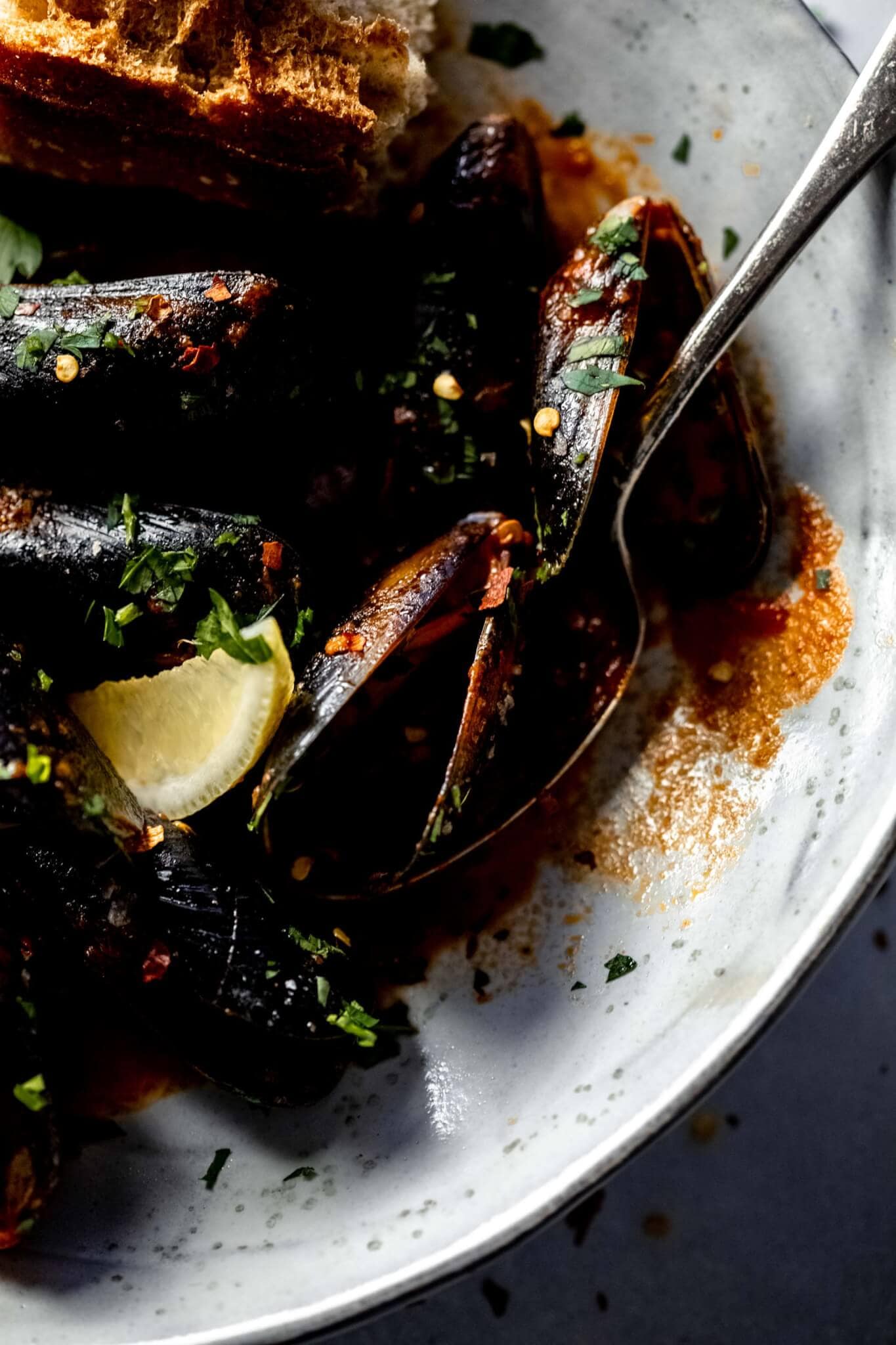 Mussels in large grey bowl after cooking served with lemon wedges.