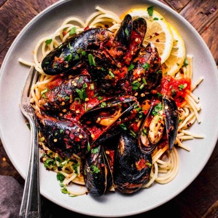 Mussels marinara served over bowl of spaghetti.