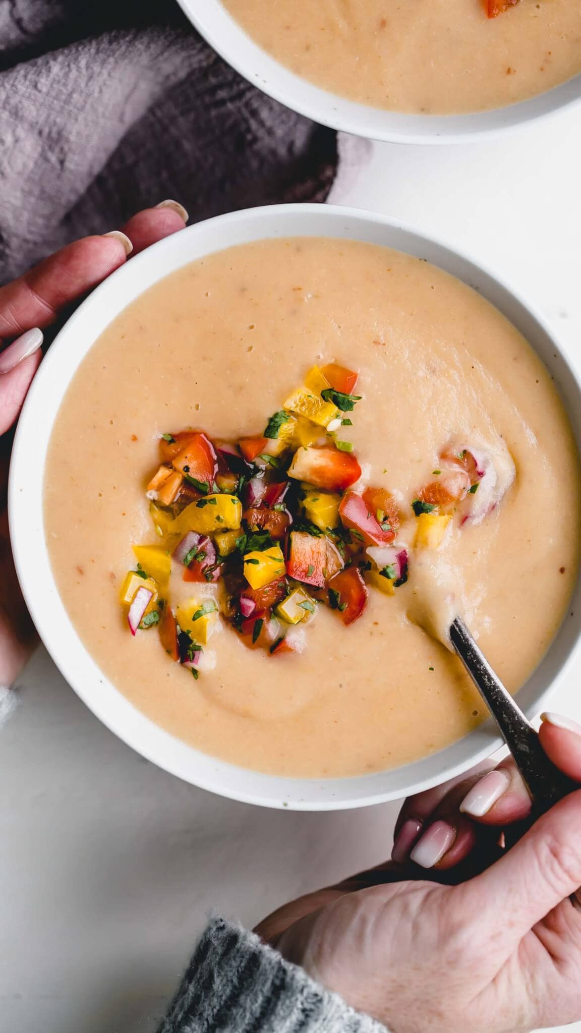 Two hands holding bowl of potato cheese soup.