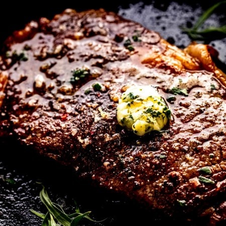 Side view of sous vide ribeye steak in cast iron skillet topped with compound butter.