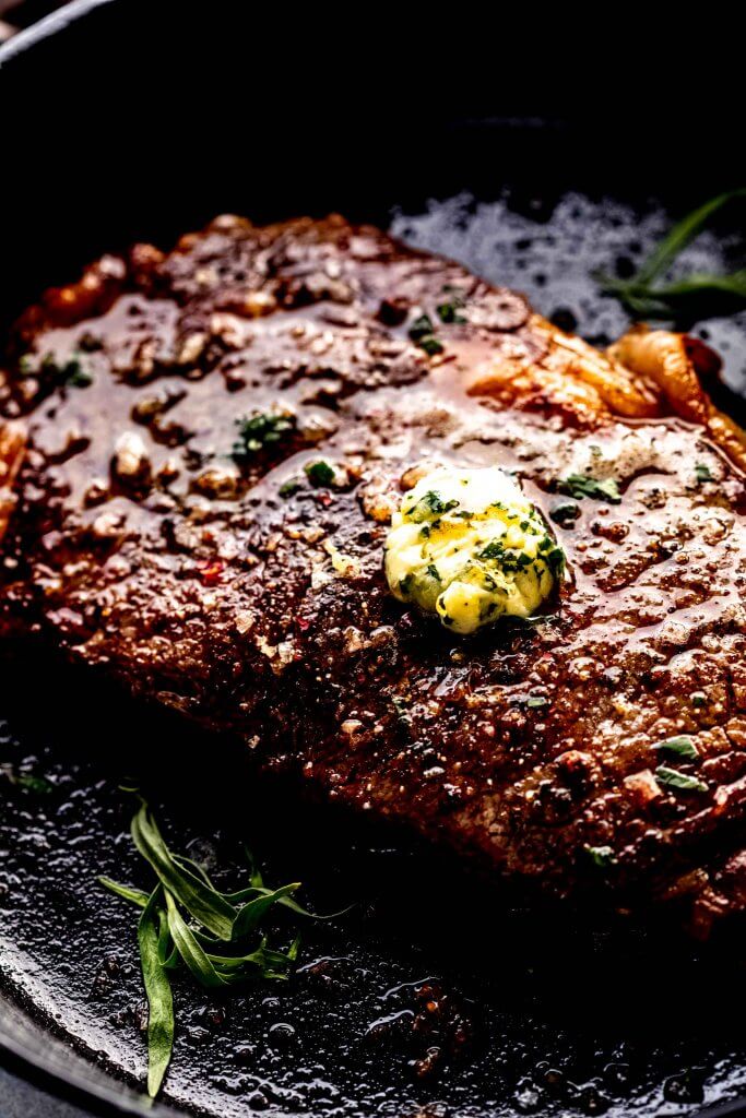 Side view of sous vide ribeye steak in cast iron skillet topped with compound butter.