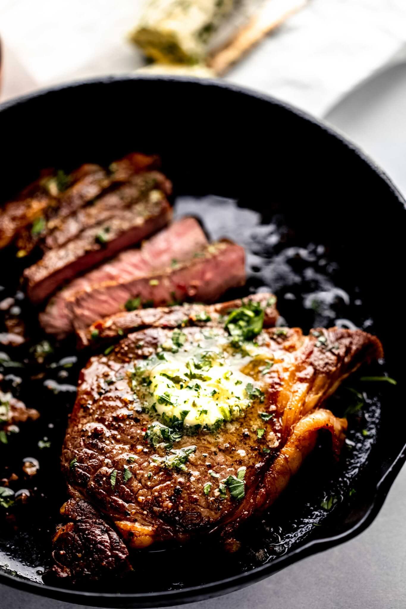 Seared ribeye in skillet sliced and topped with butter.