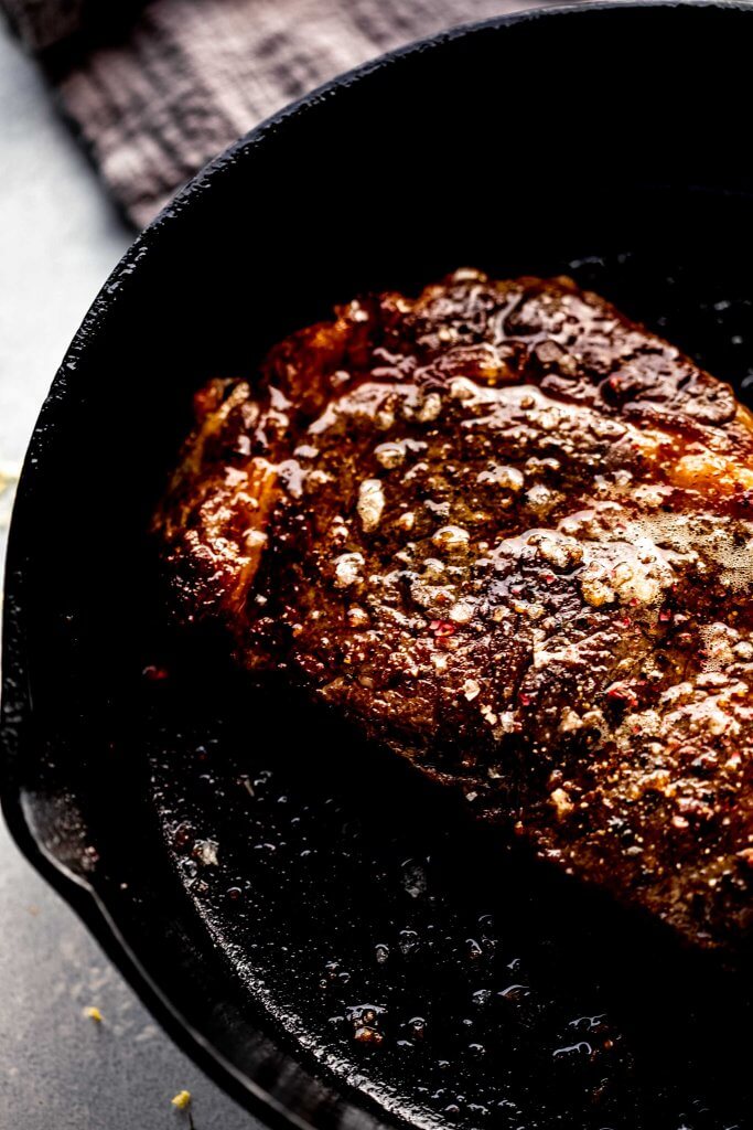 Ribeye being seared in skillet.