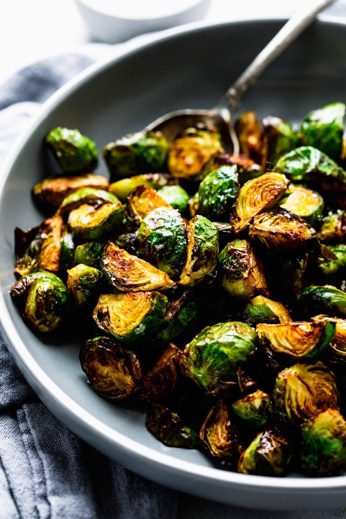 Side view of bowl of air fried brussel sprouts in grey bowl with spoon.