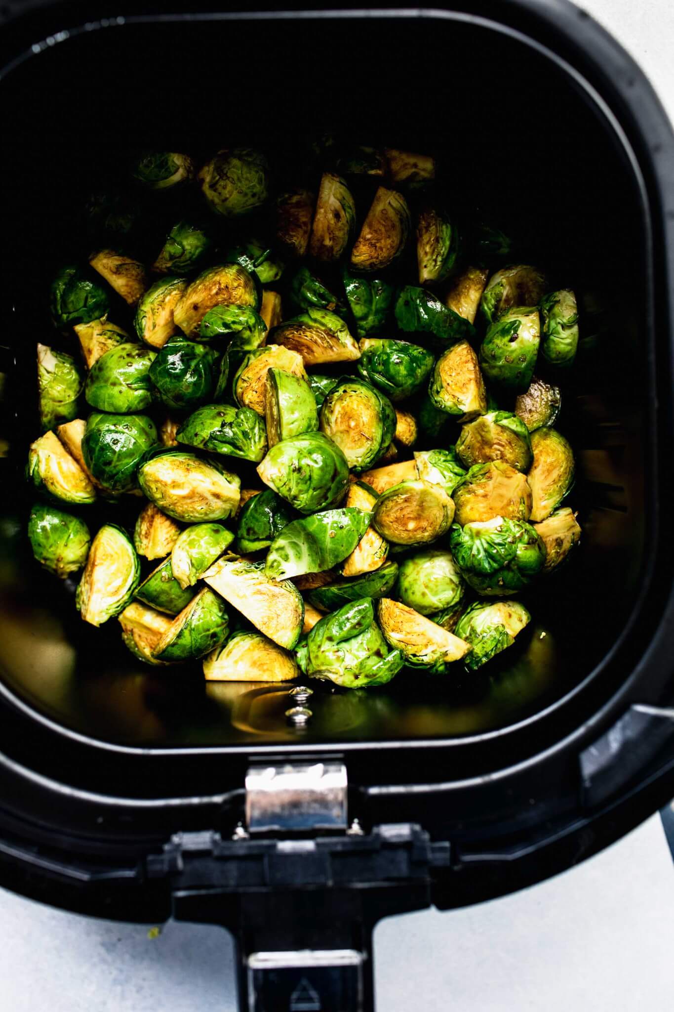 Uncooked brussels sprouts in air fryer basket.