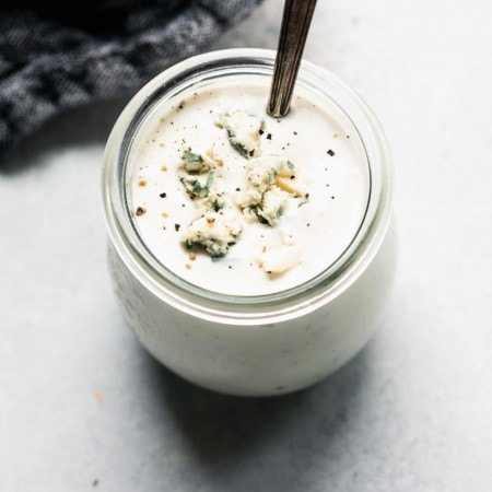 Side view of container of blue cheese dressing in small jar with spoon.