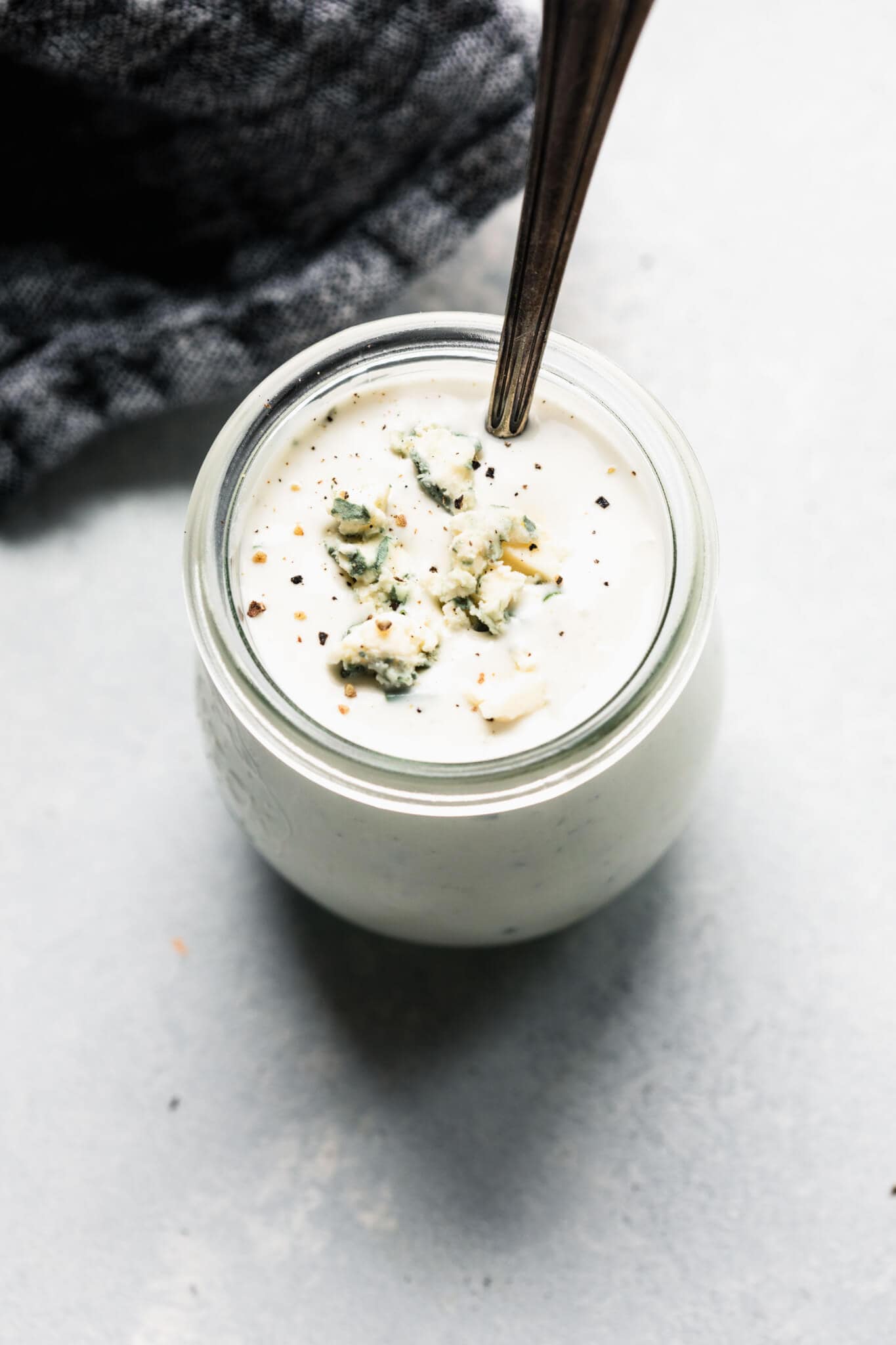 Side view of container of blue cheese dressing in small jar with spoon.