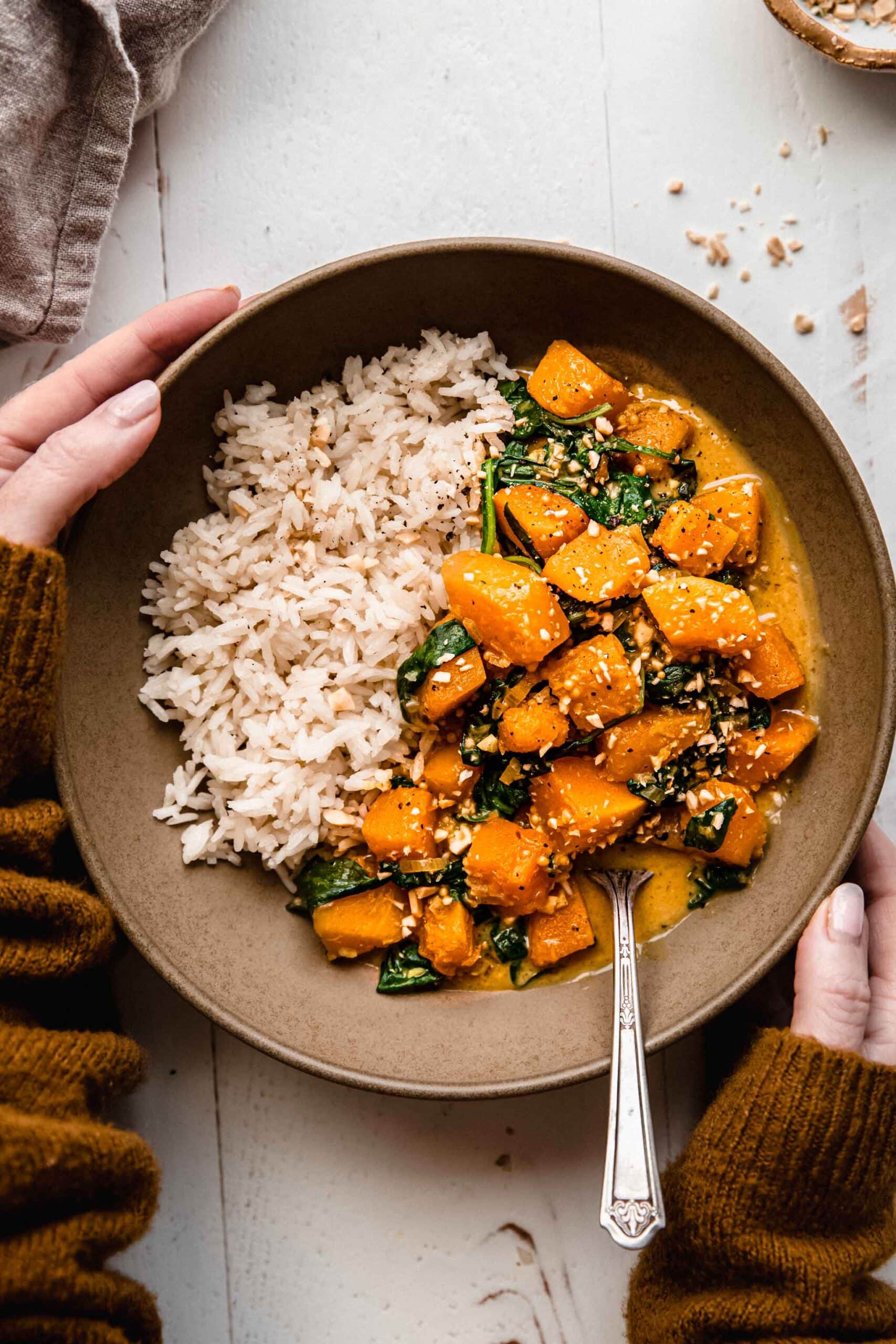 Hands holding bowl of butternut squash curry.