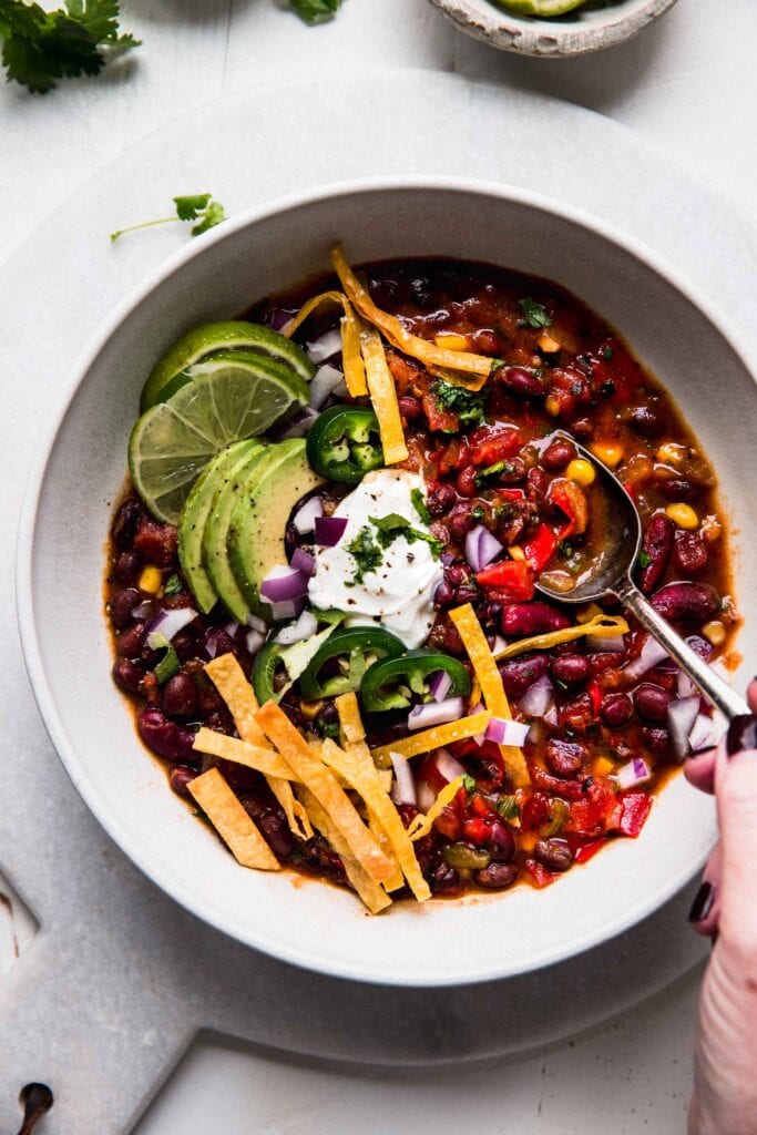 HAND HOLDING SPOON DIPPING INTO BOWL OF VEGGIE CHILI. 