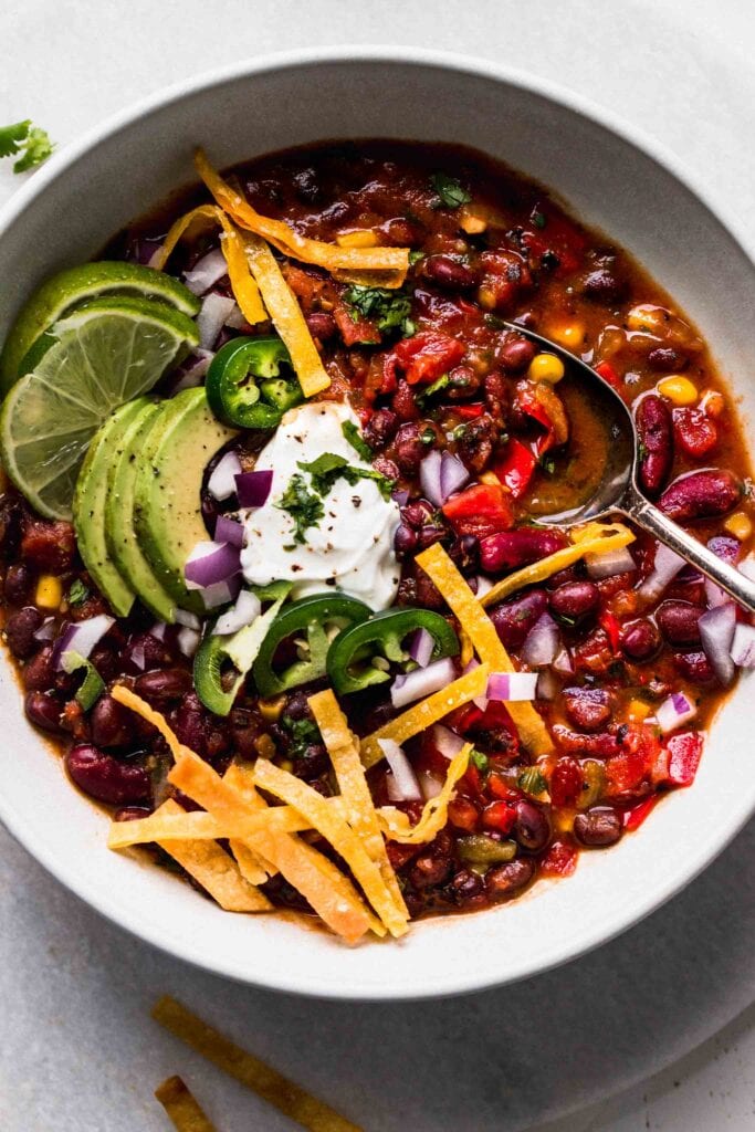 OVERHEAD CLOSE UP OF BOWL OF INSTANT POT VEGETARIAN CHILI WITH SOUR CREAM, AVOCADO, TORTILLA STRIPS.