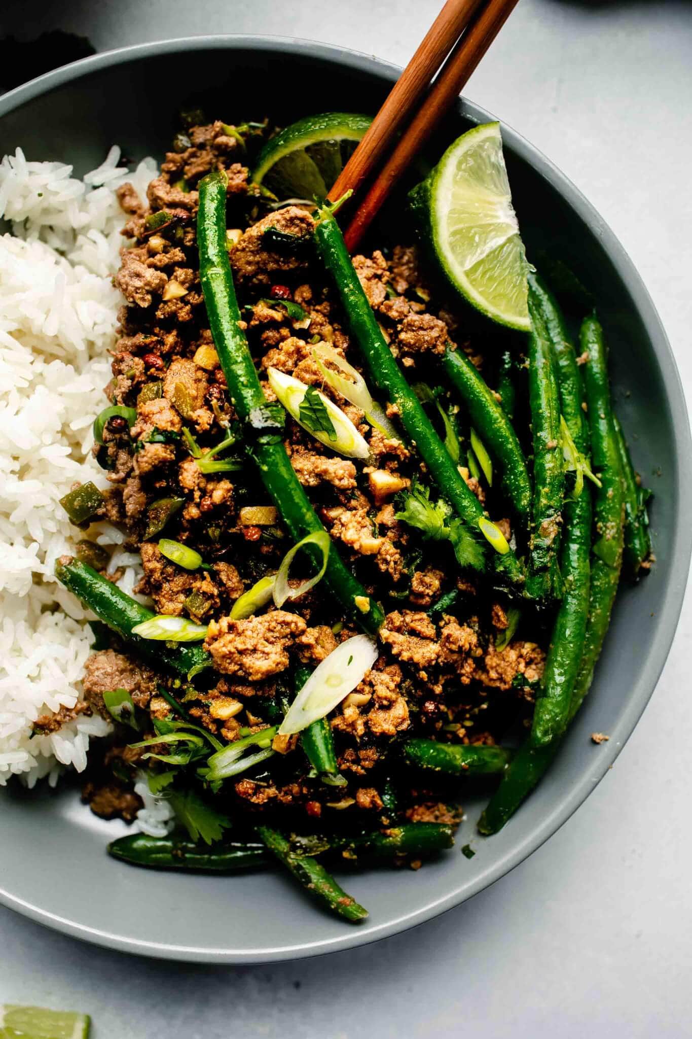 Overhead close up of lamb curry in bowl with chopsticks and lime wedges. 