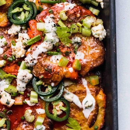 Overhead shot of smashed potatoes on baking sheet topped with blue cheese, hot sauce, jalapenos and chives.