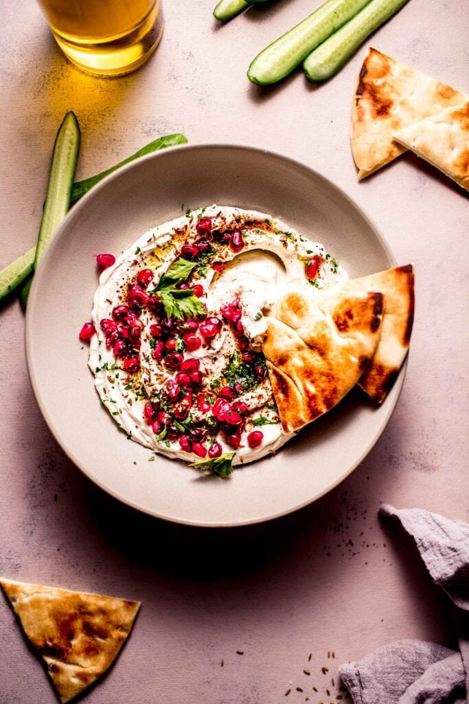 Bowl of yogurt tahini sauce with pita dipped into it. 