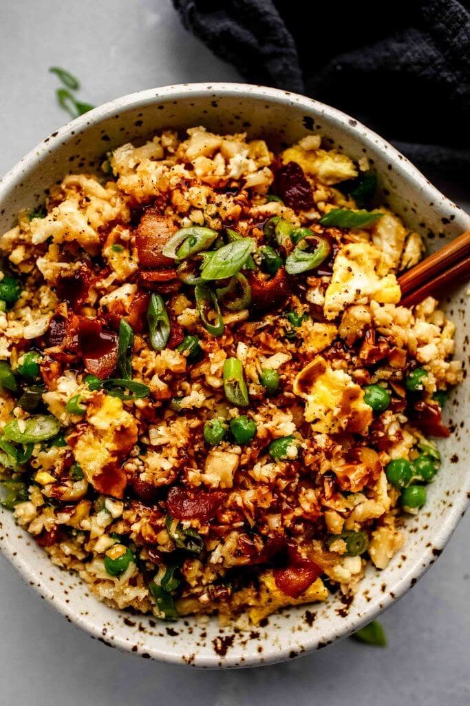 Overhead shot of cauliflower fried rice in speckled bowl with chopsticks.