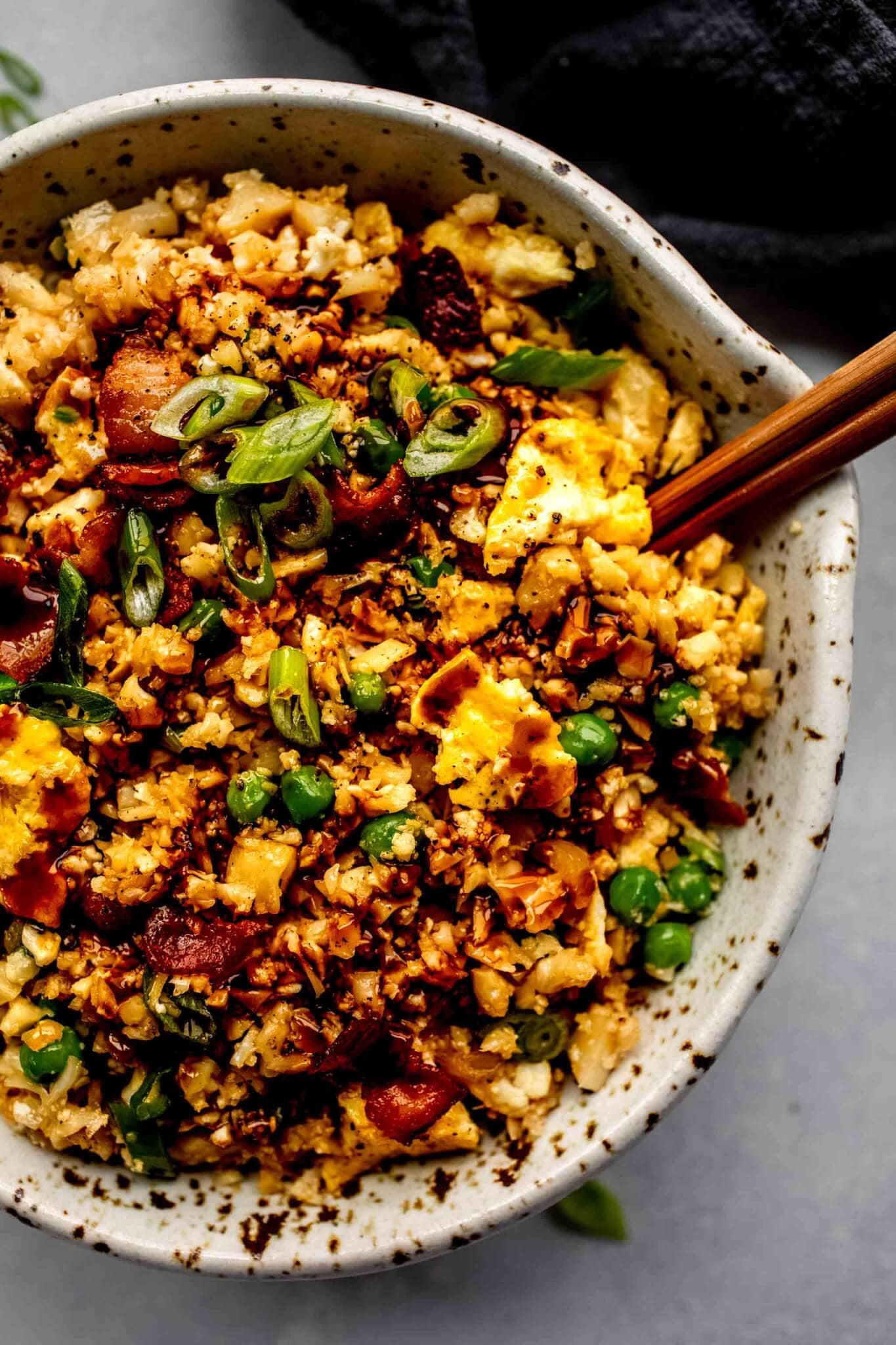 Overhead shot of cauliflower fried rice in speckled bowl with chopsticks.