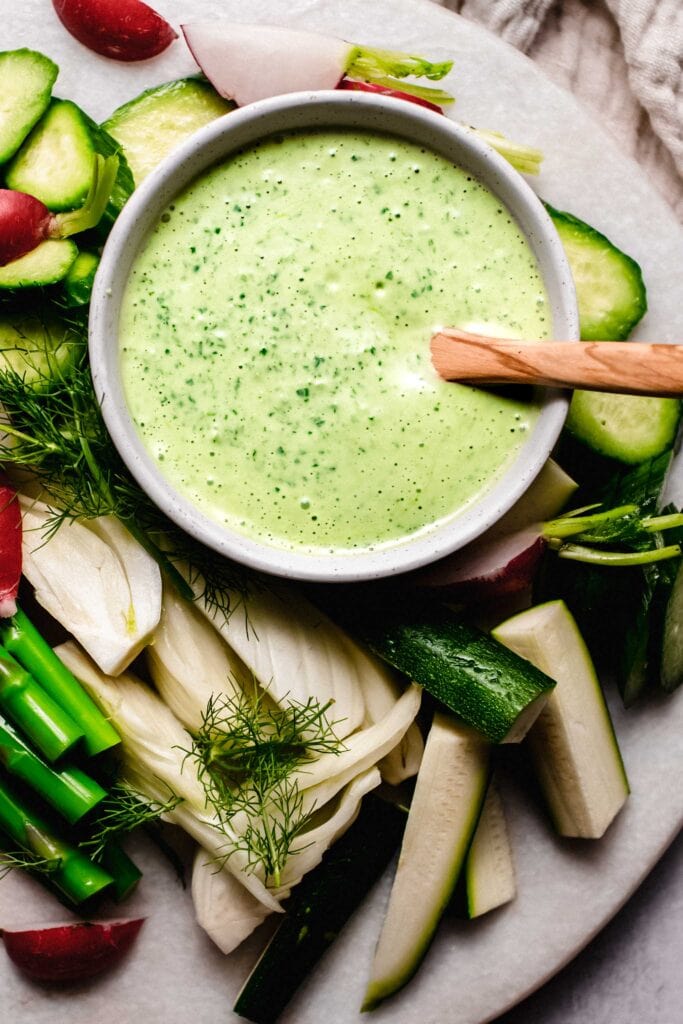 Green goddess dip in bowl with wooden spoon.