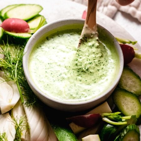 Hand holding spoon dipping into green goddess dressing.