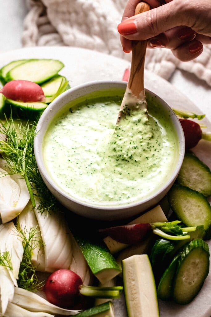 Hand holding spoon dipping into green goddess dressing.