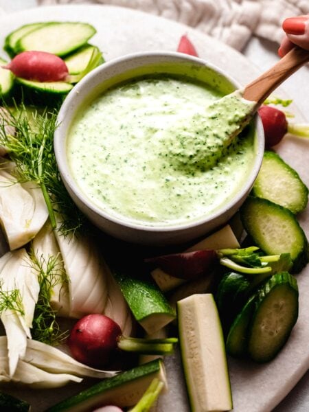 Hand holding spoon dipping into green goddess dressing.