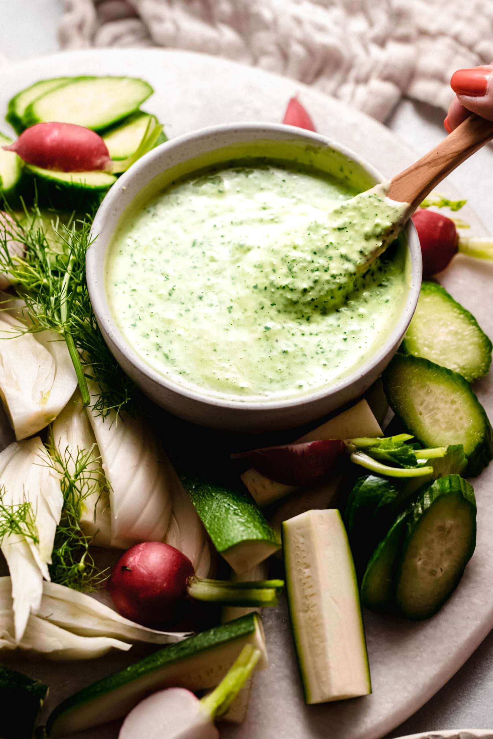 Hand holding spoon dipping into green goddess dressing.