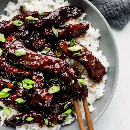 Overhead shot of mongolian beef served in grey bowl sprinkled with green onions.