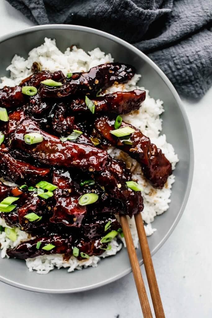 Overhead shot of mongolian beef served in grey bowl sprinkled with green onions.