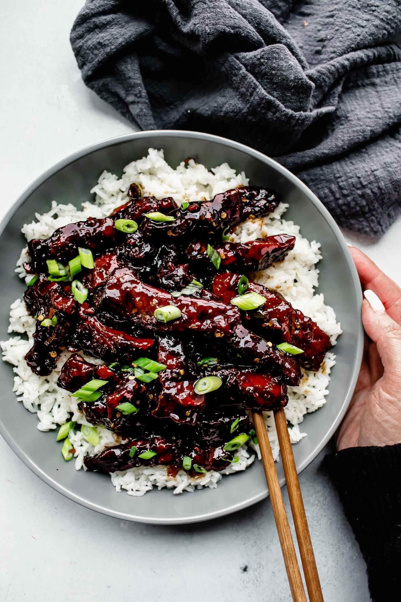 Hand holding bowl of mongolian beef.