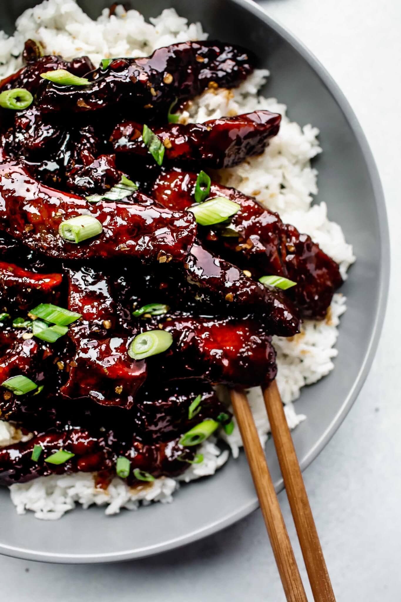 Overhead shot of mongolian beef served in grey bowl sprinkled with green onions.