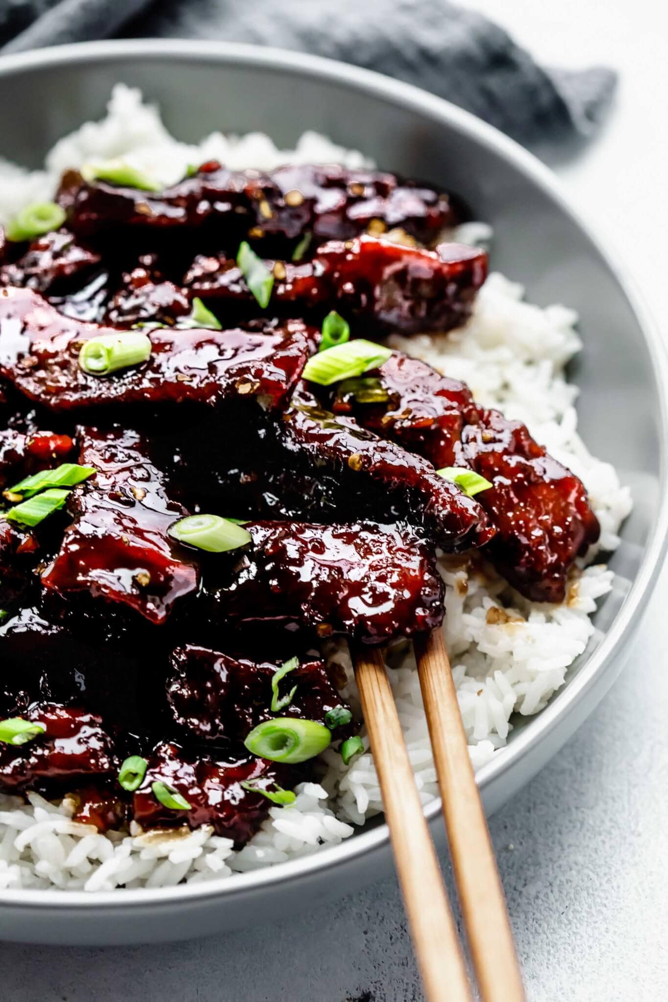 Side view of mongolian beef served on top of rice in grey bowl with chopsticks.