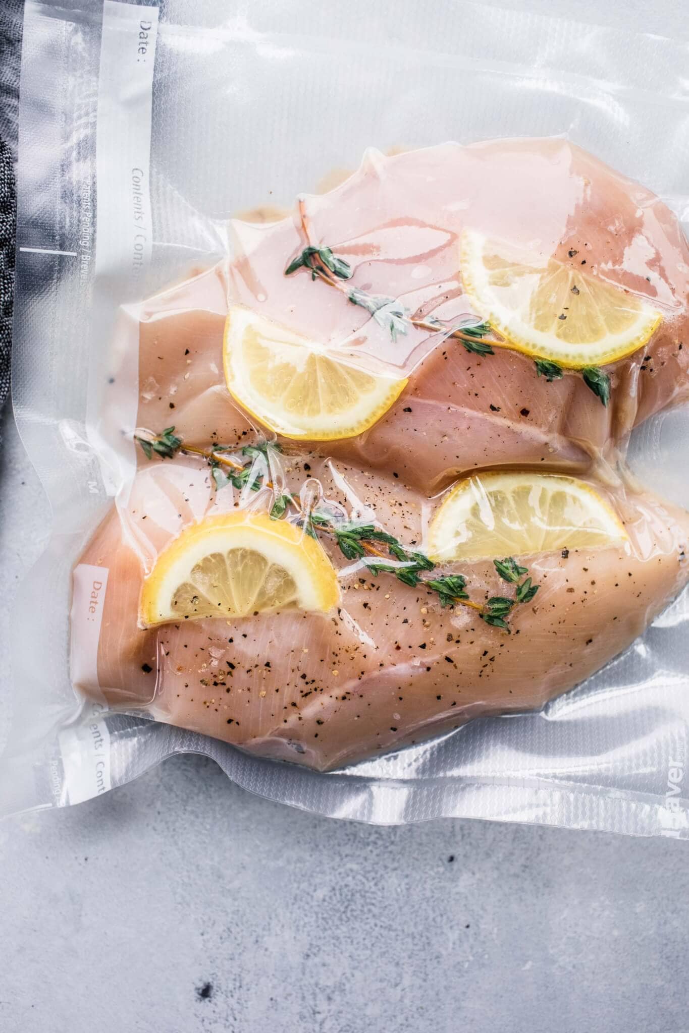 Two chicken breasts in vacuum seal bag with lemons and herbs.