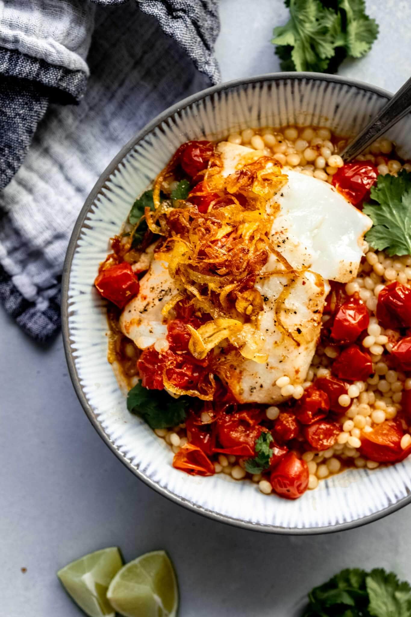 Overhead shot of poached fish in grey bowl served on a bed of couscous and topped with crispy shallots & garlic.